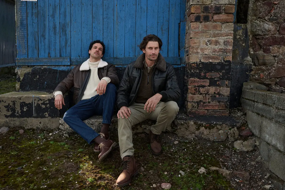 Two men in leather jackets sitting in front of a blue painted wooden wall